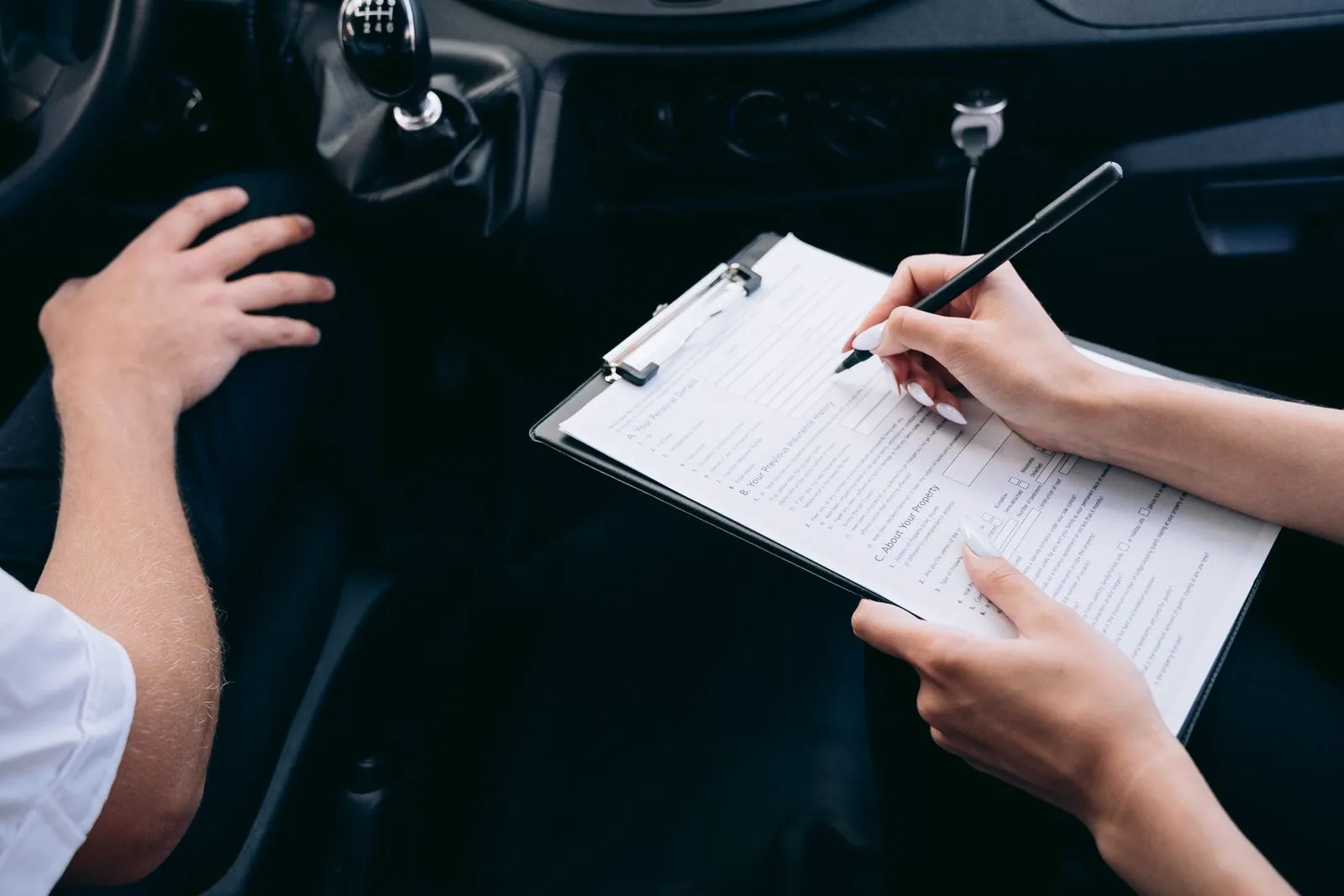 Person filling out an insurance claim form on a clipboard after a car accident